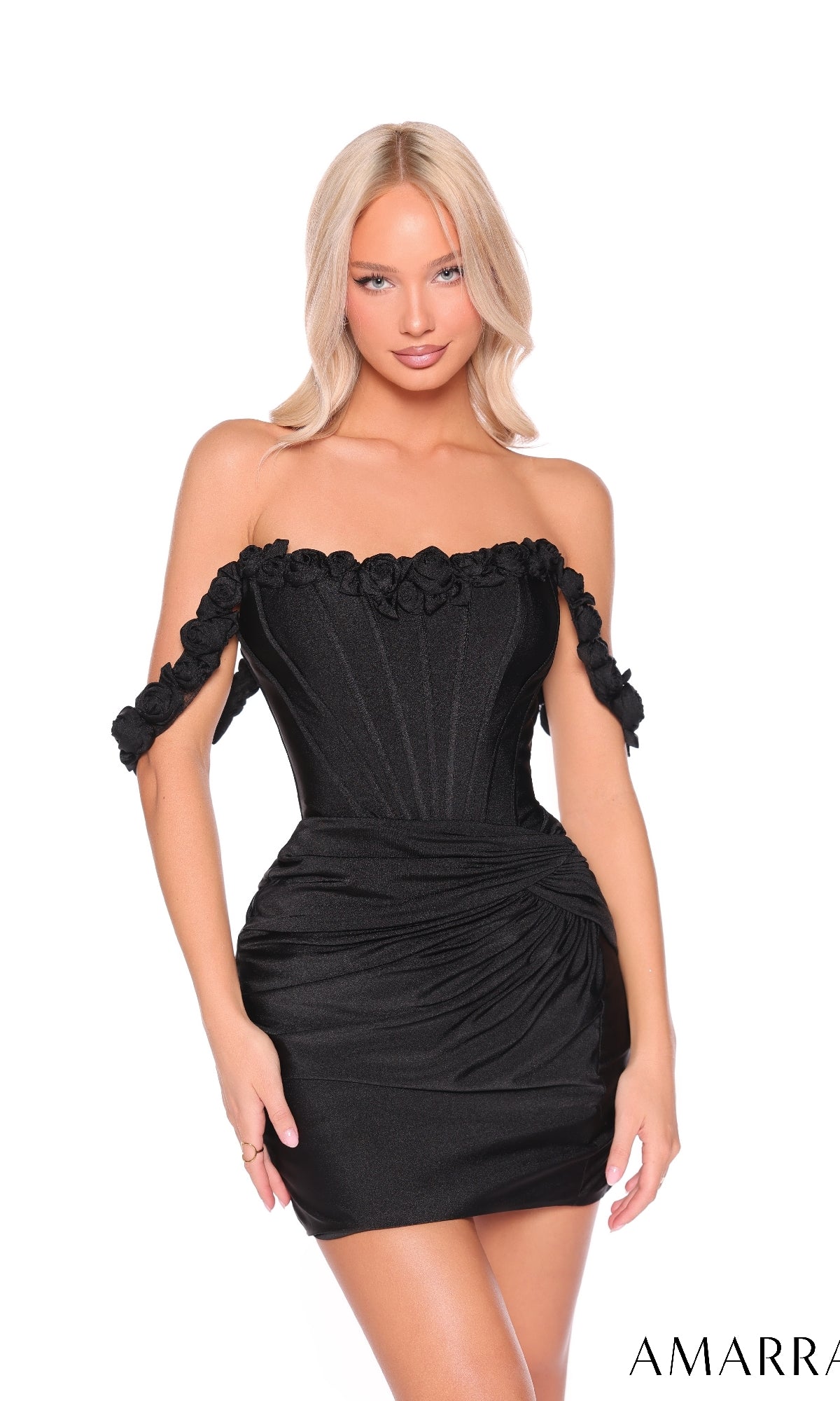 A woman with long blonde hair wears the Off-Shoulder Lace-Up Mini Hoco Dress: Amarra 88980—a black, fitted mini dress with floral details and a corset-style bodice—posing against a white background.